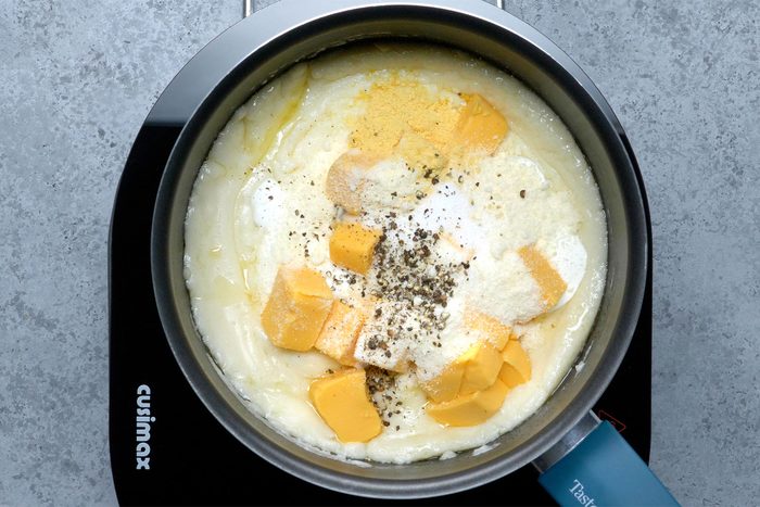 Overhead shot of a same saucepan; stir in sour cream; velveeta; parmesan cheese; salt; mustard and pepper until smooth and cheese is melted; induction; grey marble texture background;