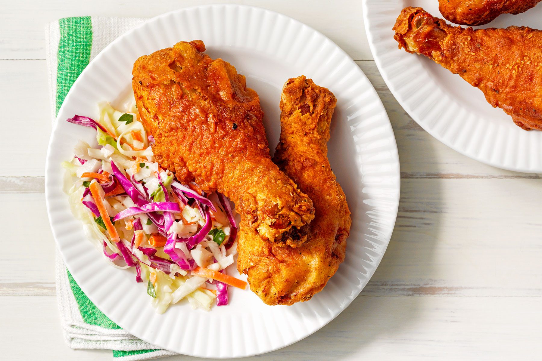 Overhead shot of Deep-Fried Chicken Legs; served on two white plates; with salad; napkin; wooden background;