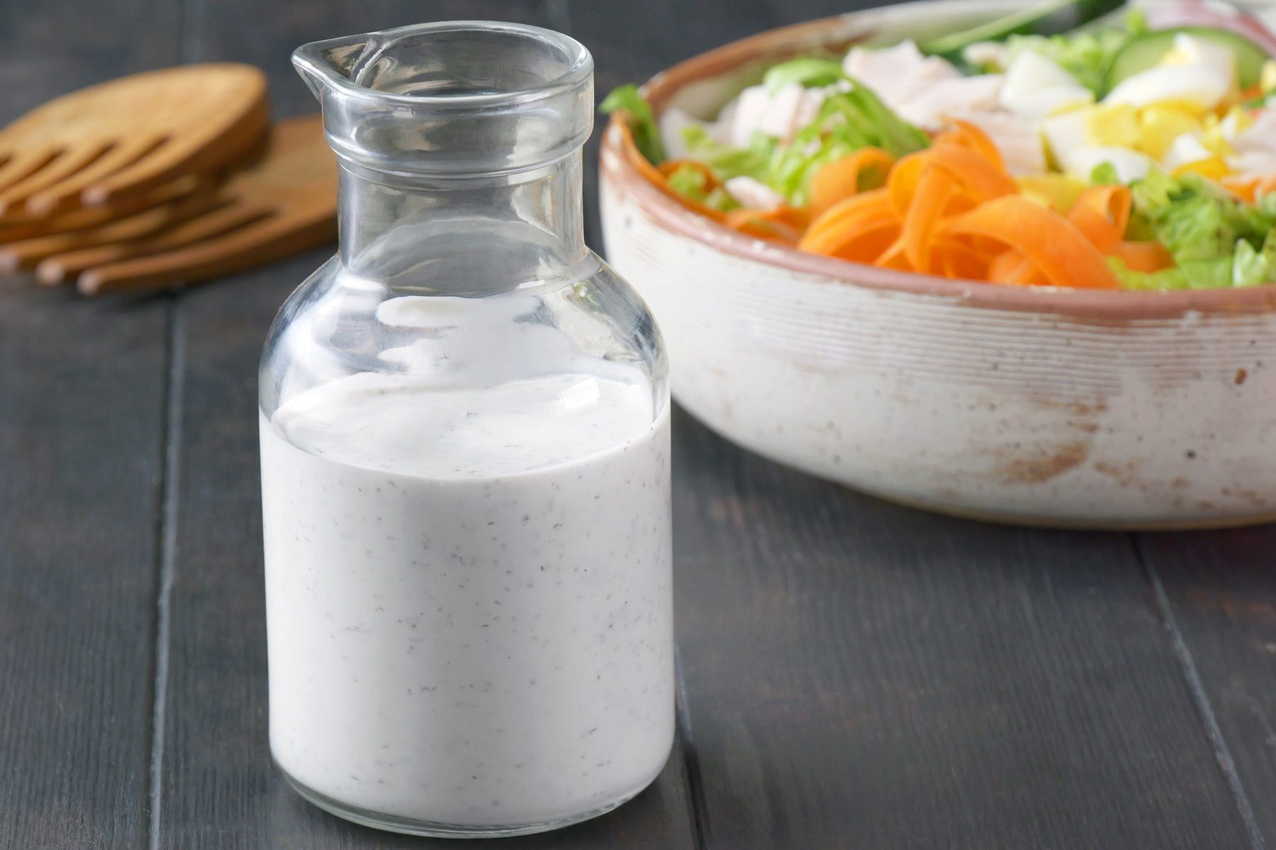 A glass container of Homemade Ranch Dressing with a bowl of salad