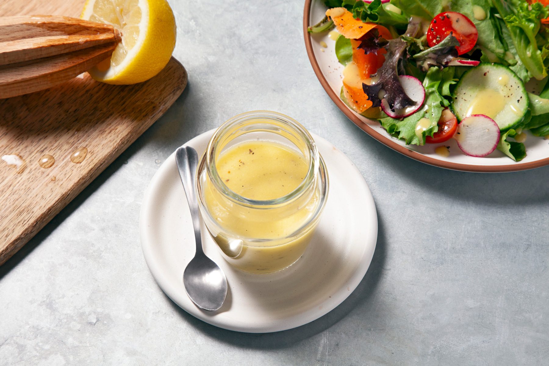A jar of Lemon Vinaigrette dressing on a plate with a spoon