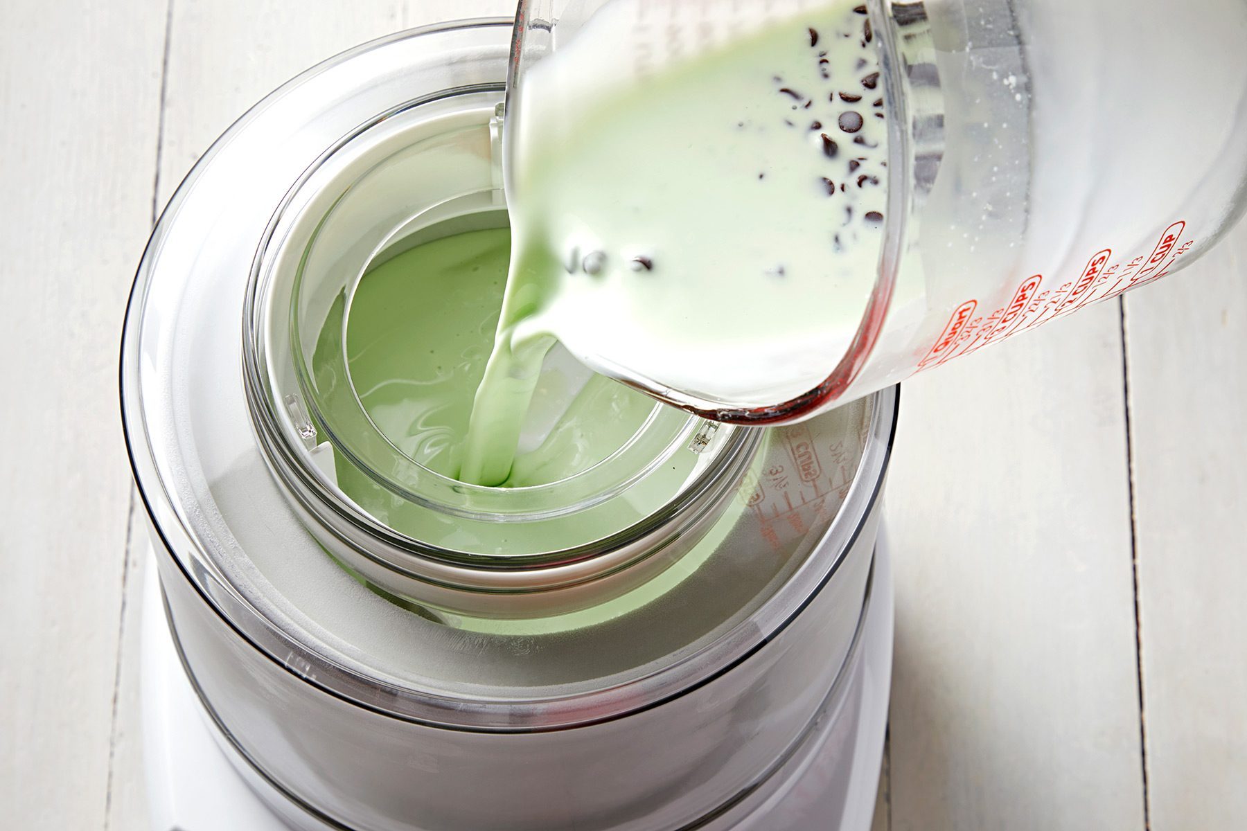 3/4th shot; white background; pouring ice cream mixture into ice cream maker;