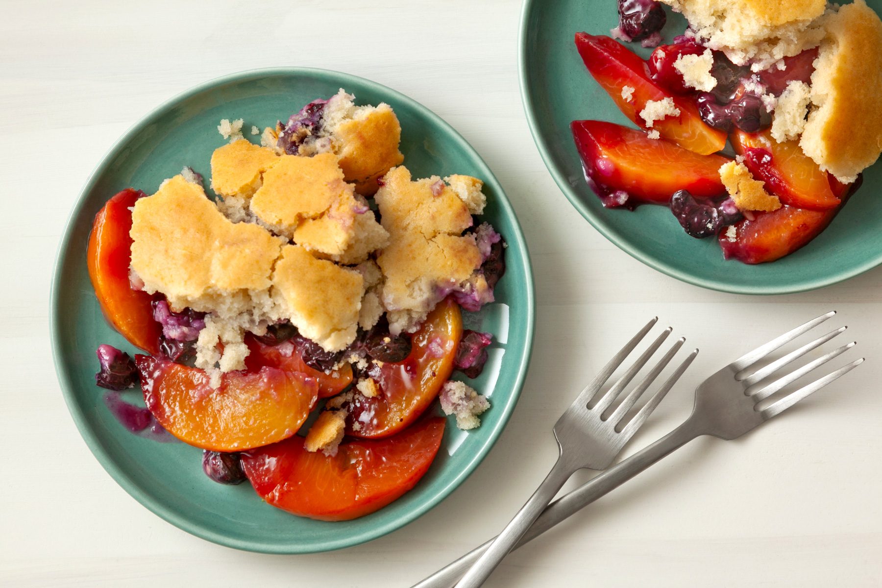 Two plates of Peach Blueberry Cobbler along with forks on a table