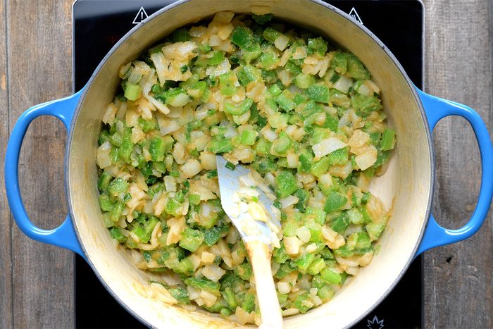 Overhead shot of added the onion; celery; green pepper and green onions in a dutch oven; cook and stir for 5 minutes; spatula; wooden background;