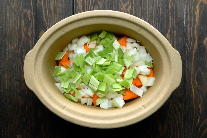 A slow cooker filled with chopped potatoes, carrots, onion and celery.