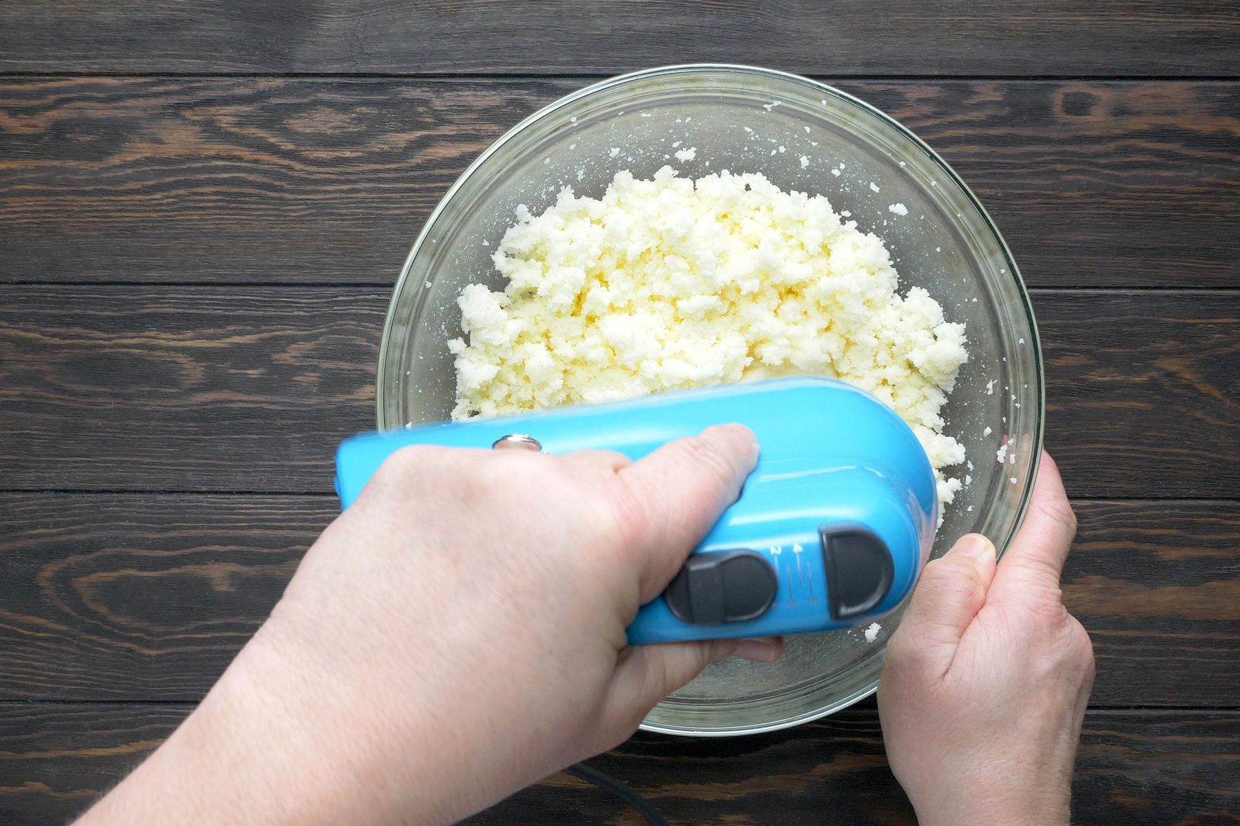 A person is creaming the butter and sugar in a bowl using a electric hand mixer.