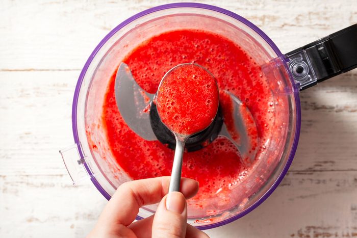 overhead shot of strawberries in a food processor Processed until pureed; white wooden background;