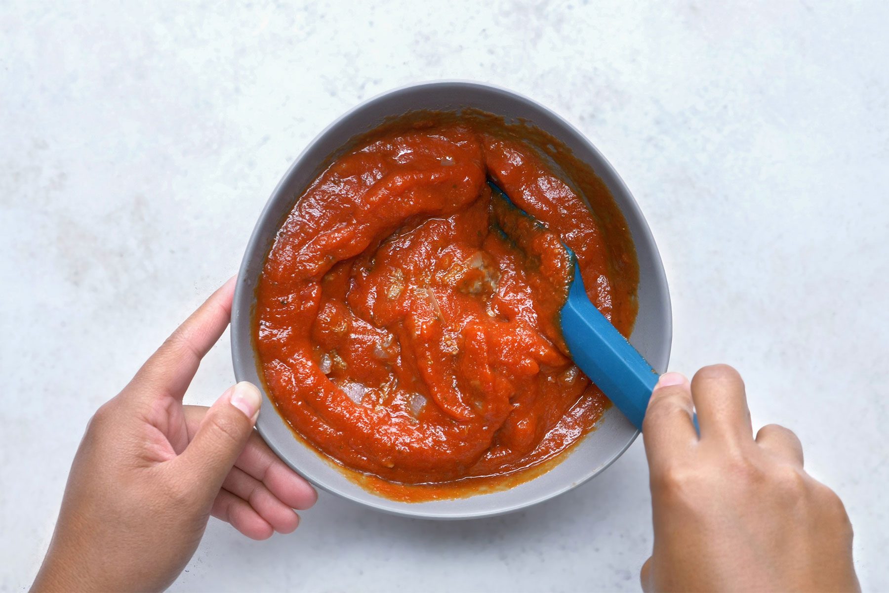 overhead shot; white background; Combining beef mixture and spaghetti sauce using spatula;