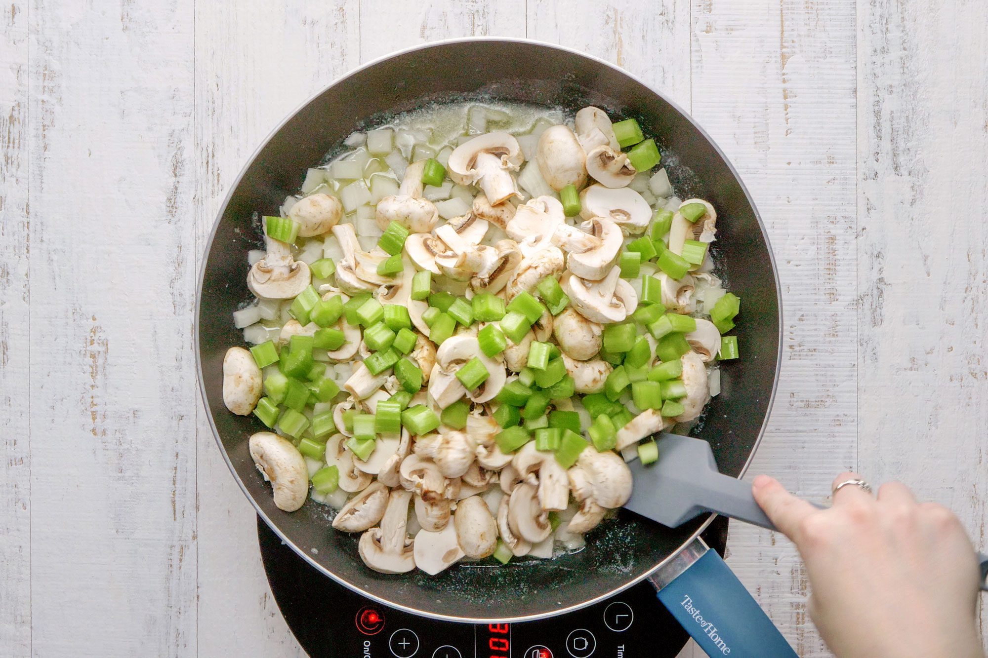overhead shot of sauteing the onions, celery and mushrooms in a large skillet; wooden background;