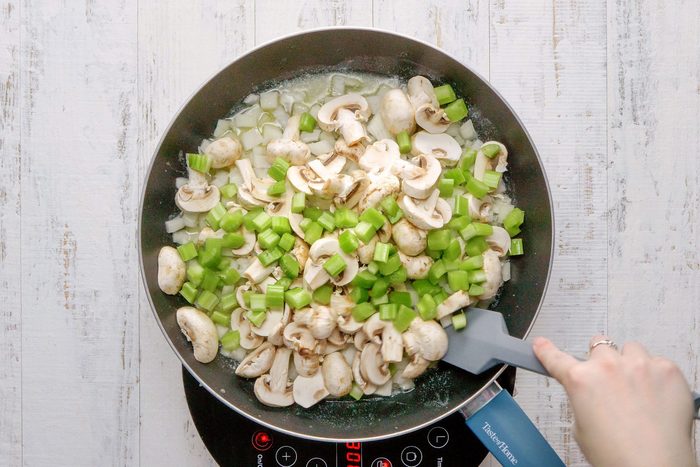overhead shot of sauteing the onions, celery and mushrooms in a large skillet; wooden background;