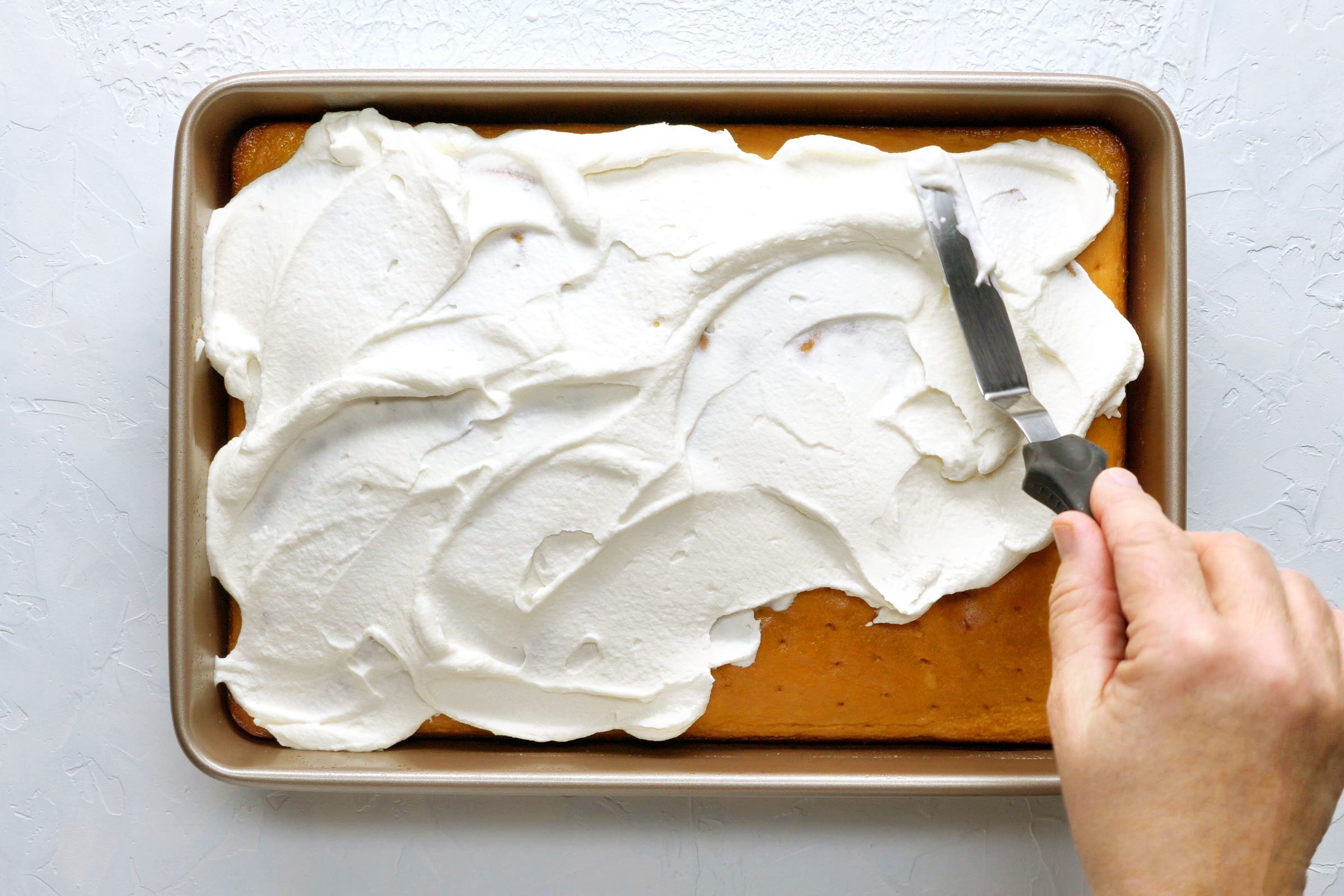 putting whipped cream on tres leches cake