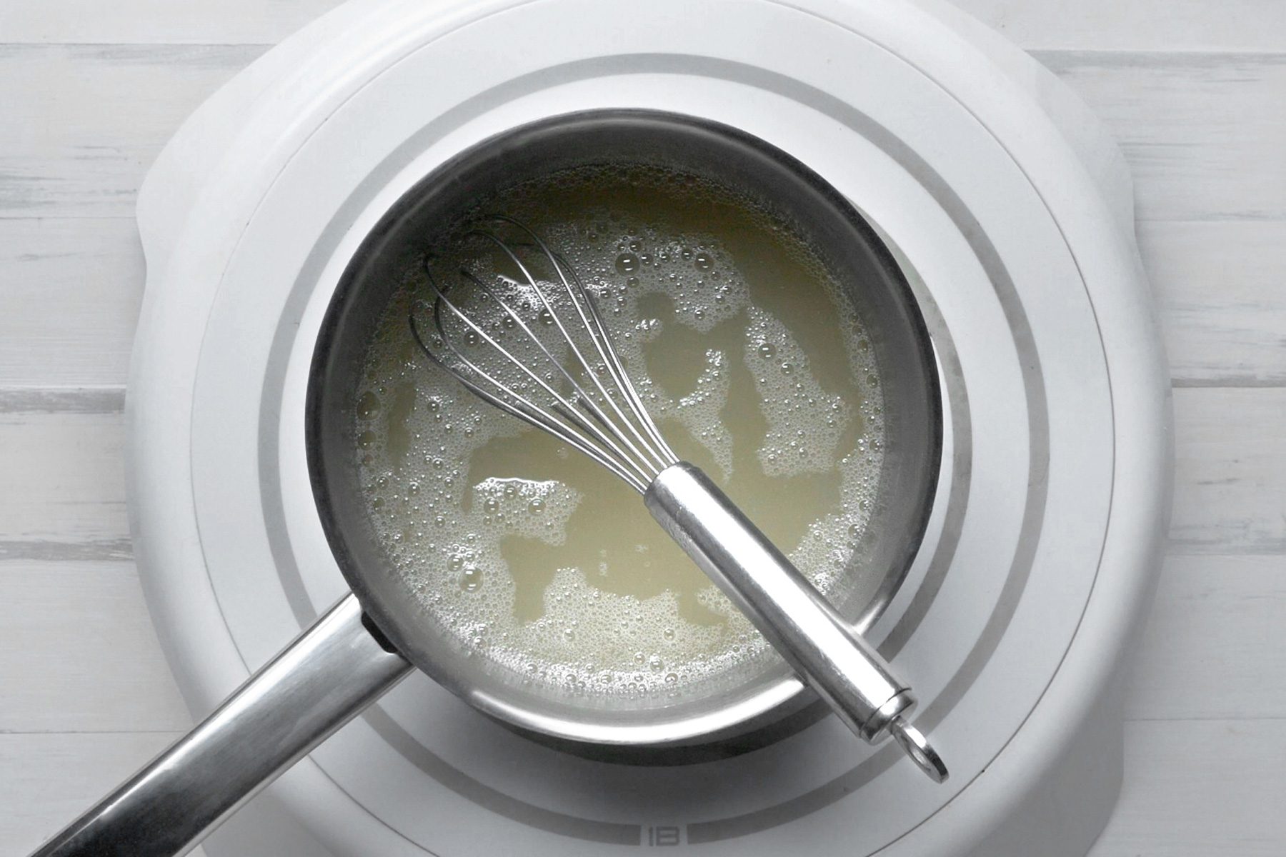 A whisk in a small saucepan of syrup on a white table.