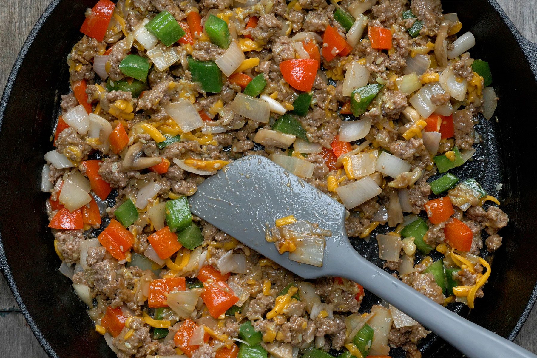 Close shot of remove skillet from heat; added 1/2 cup cheese, ketchup, salt and pepper; mix well; spatula; wooden background;