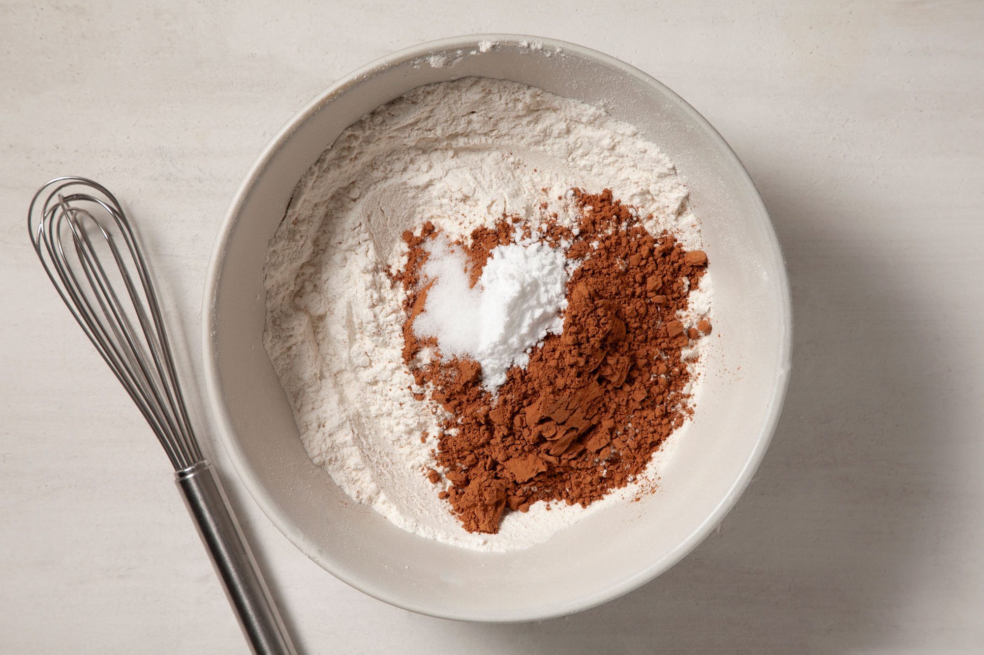 Overhead shot of a bowl; combine flour; cocoa; baking soda and salt; whisk tool; marble background;