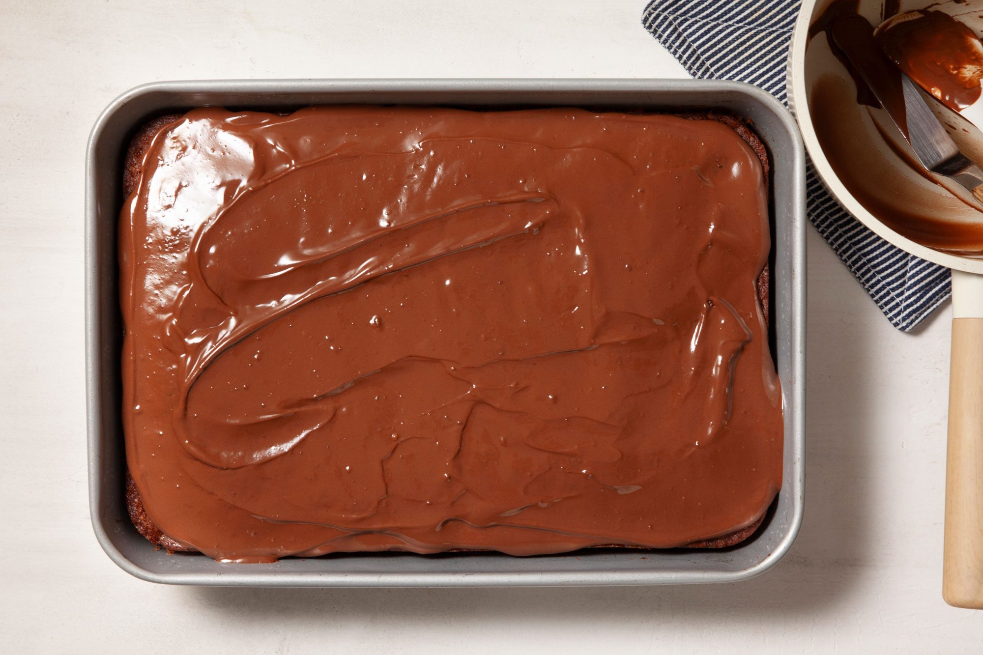 Overhead shot of a baking pan; spread over warm brownies; kitchen towel; marble background;
