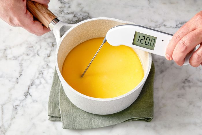 wide shot of digital thermometer reading temperature of a yellow liquid in a white saucepan