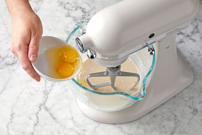 wide shot of pouring two eggs into a glass bowl; stand mixer; marble surface;