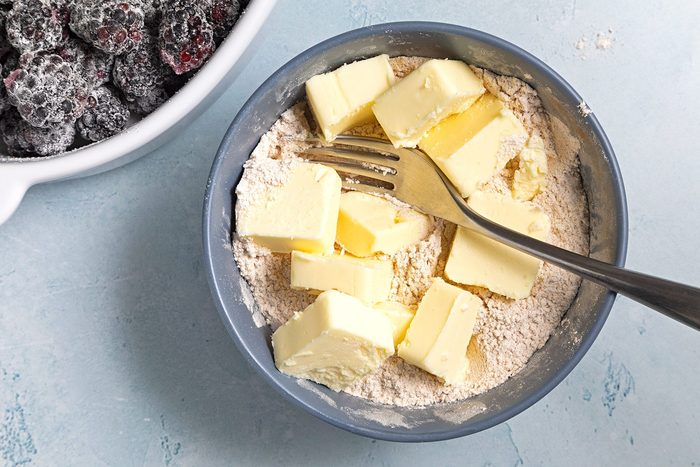 Overhead shot of cut butter in cubes add in mixture; fork; blue marble background