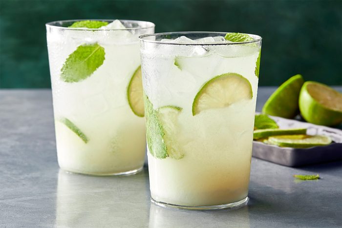 horizontal shot; green background; grey base; Coconut Mojito served into glasses garnished with additional lime and mint leaves