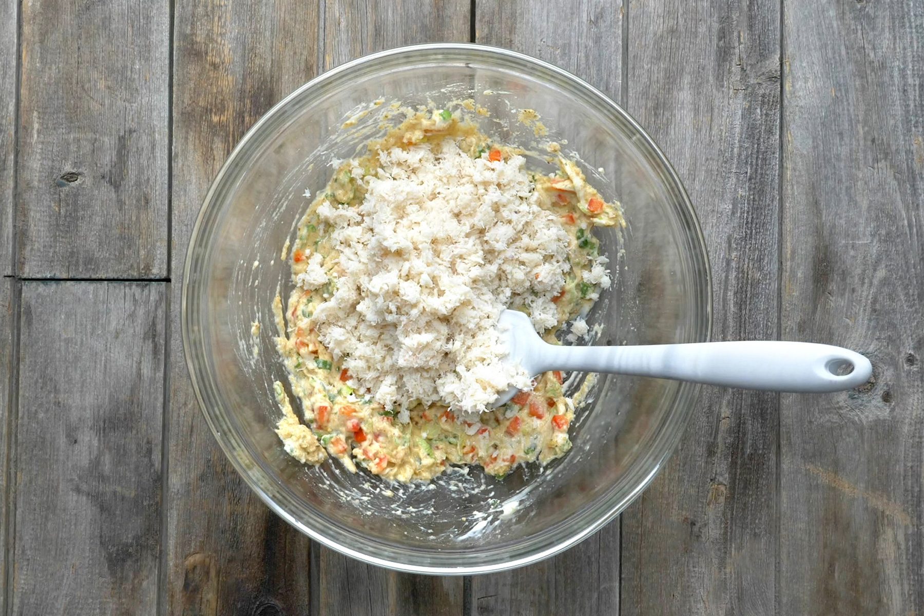 A bowl with a mixture of crabmeat, green onions, red pepper, egg, mayonnaise, and other ingredients