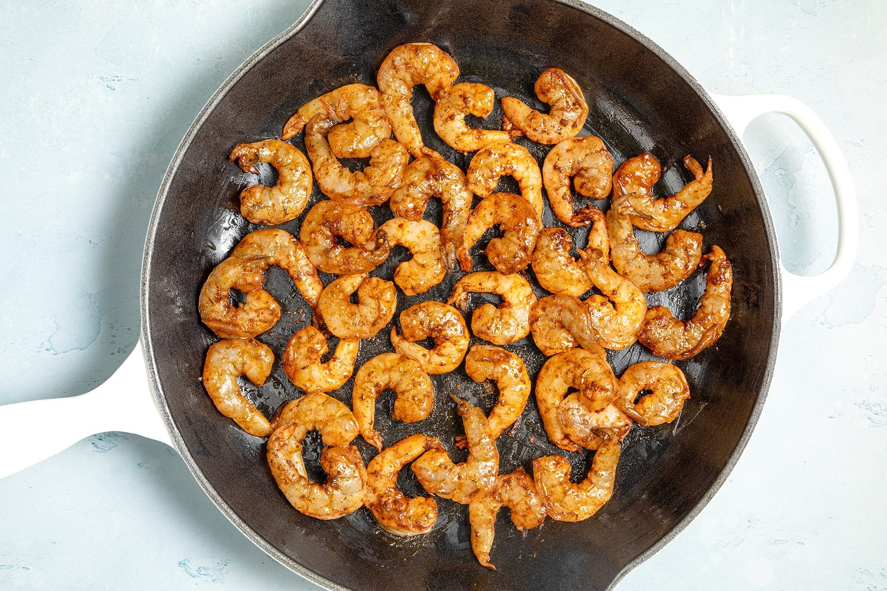 A cast iron skillet filled with cooked shrimp seasoned with spices.