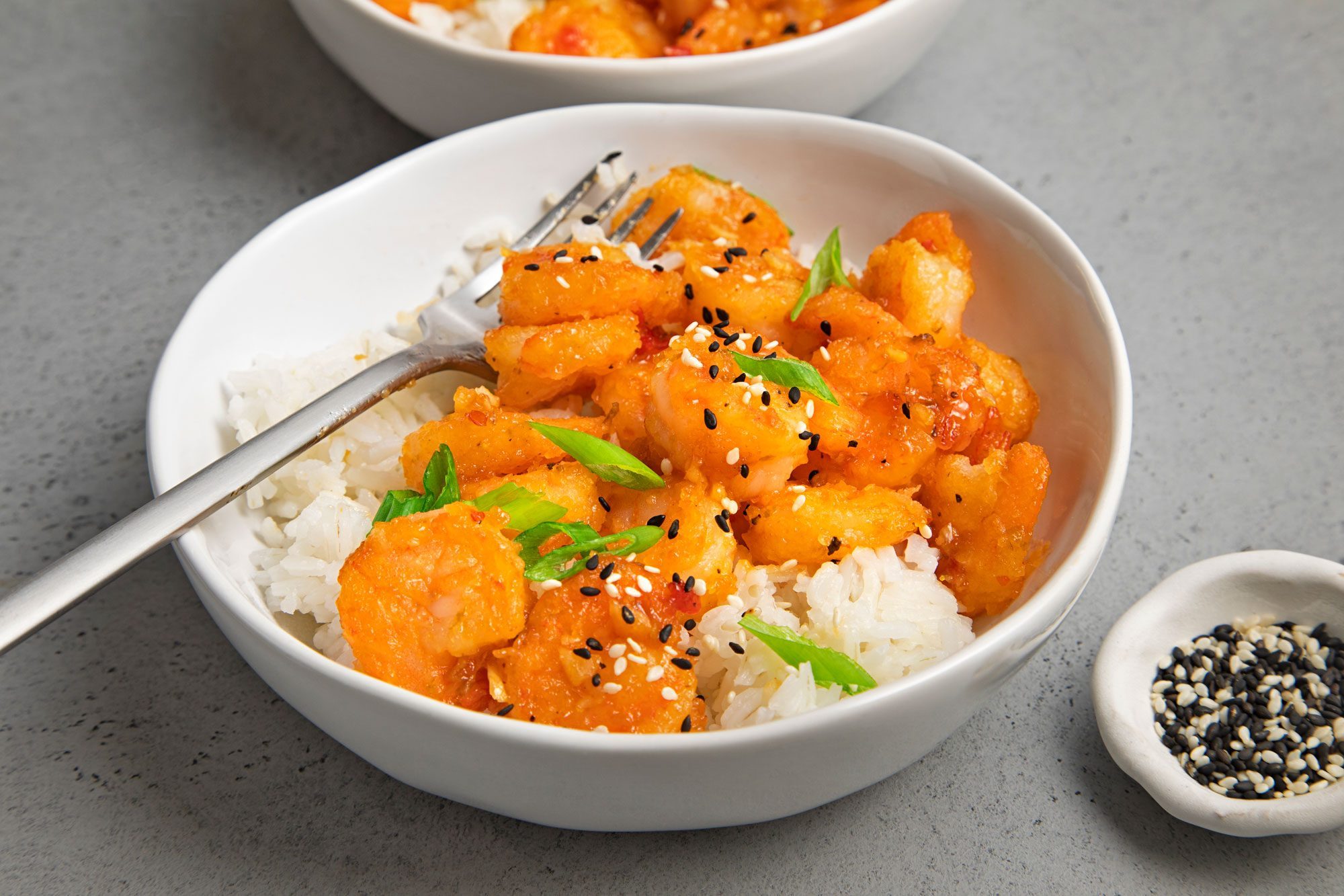 wide shot of firecracker shrimp served with rice, garnished with sesame seeds and green onions