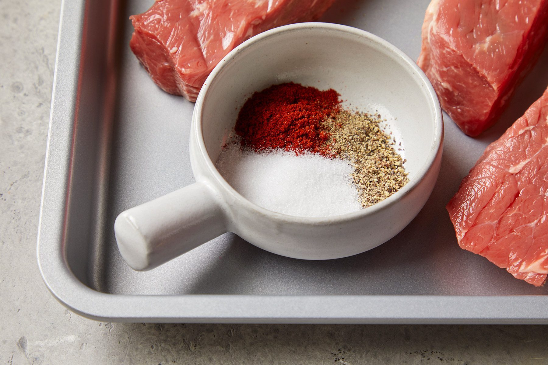 High angle view shot of a small bowl; combine 3 ingredients; ribs; baking pan; marble background
