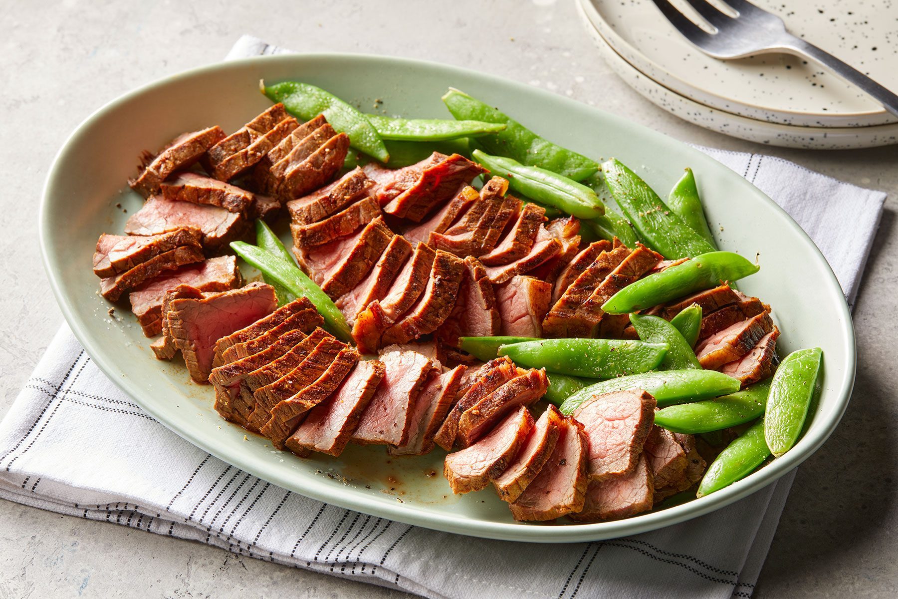 3/4 angle view shot of Grilled Short Ribs; served on large platter with beans; small plates; fork; napkin; marble background
