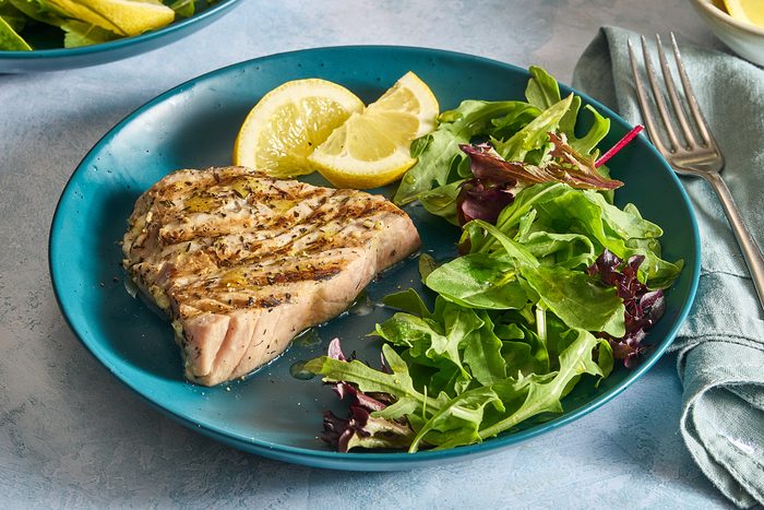 Closeup of a grilled tuna steak with salad and lemon wedges