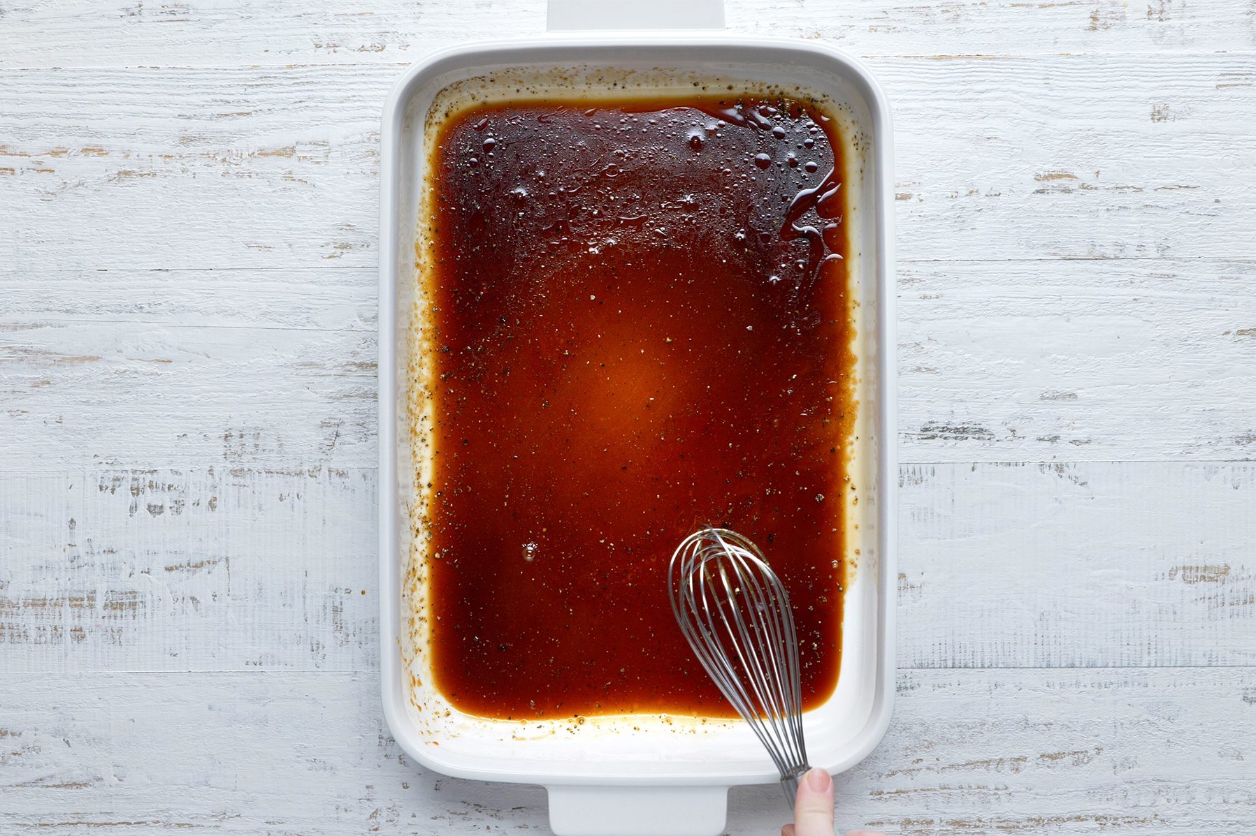 A white rectangular baking dish filled with a dark brown liquid sits on a light wooden surface. 