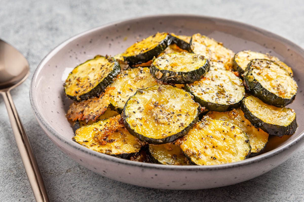 Taste of Home roasted zucchini recipe photo of roasted zucchini in a purple shallow bowl with rose gold spoon.