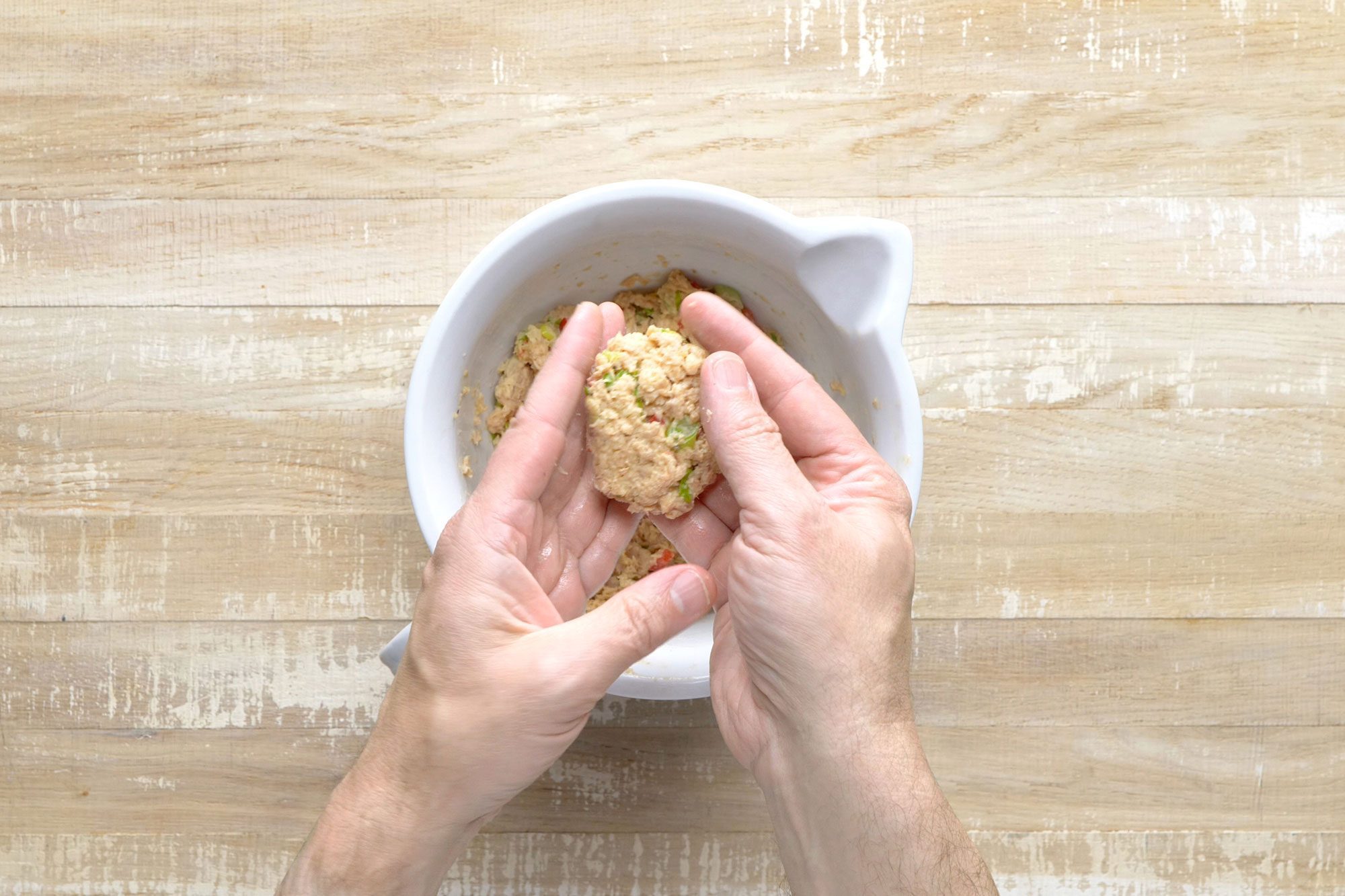 Overhead shot of shape 2 tablespoonfuls salmon mixture into 1/2-in thick patties; wooden background;