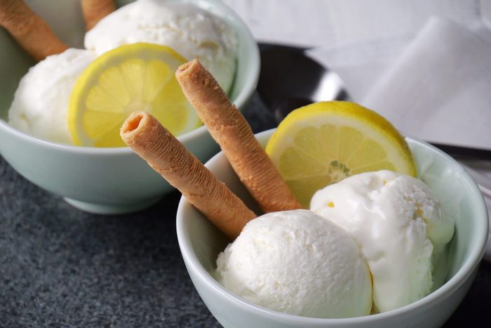 Two bowls of Simple lemon ice cream each garnished with two rolled wafer sticks and a slice of lemon.