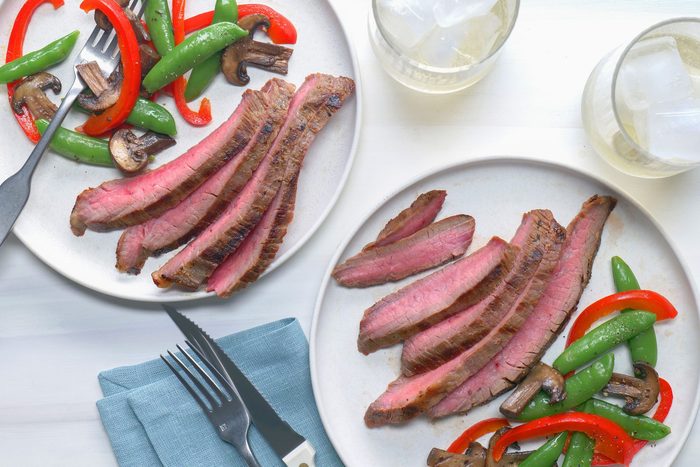 Two plates of Soy Marinated Flank Steak with vegetables elegantly presented on a table