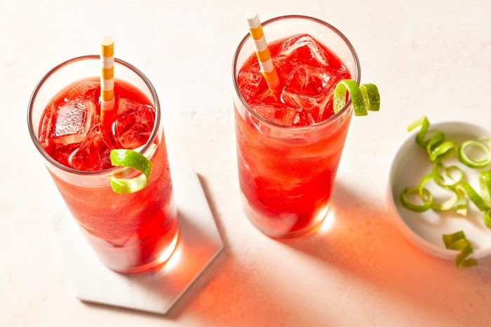 Overhead shot of Vodka Cranberry; placed ice a highball glass; poured the vodka and cranberry juice into the glass; garnished with lime twist; straws; light pink background;