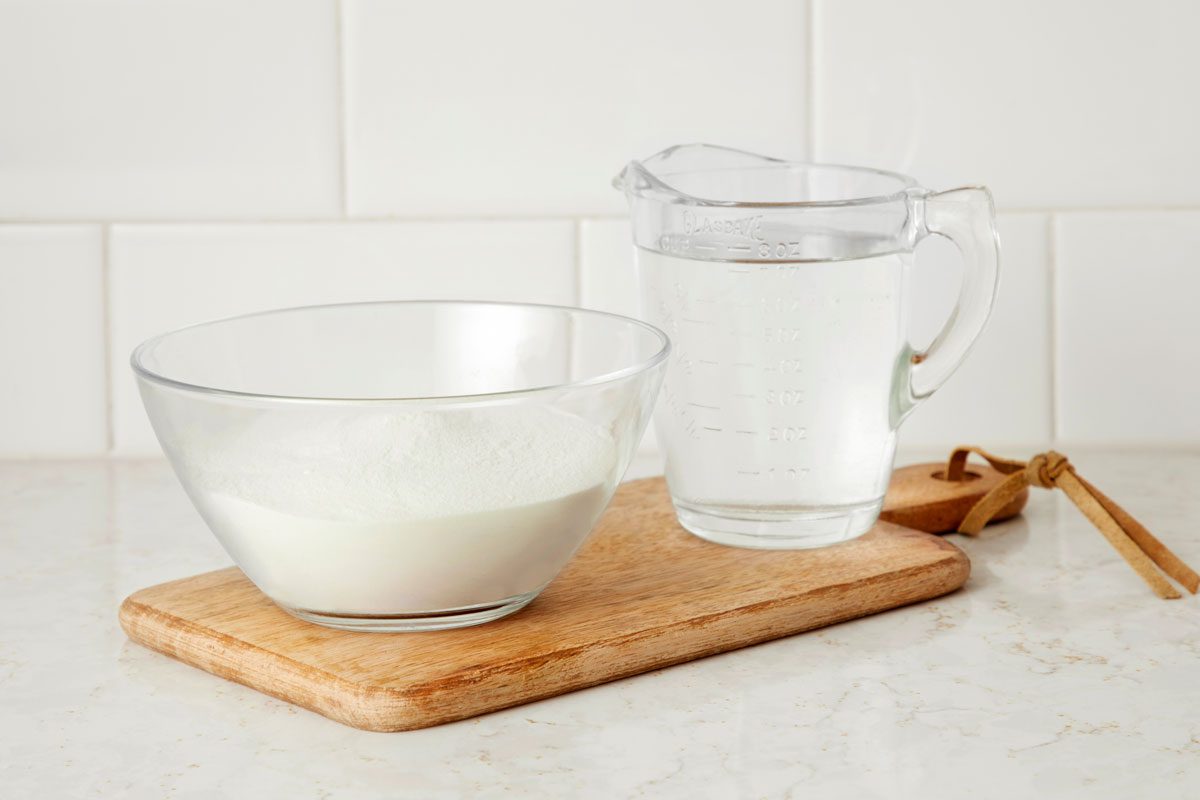 Powdered milk in a bowl next to a small pitcher of water on a kitchen counter