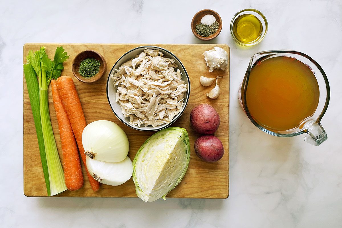Ingredients for cooking Taste of Home's Chicken Cabbage Soup on a cutting board and white marble background
