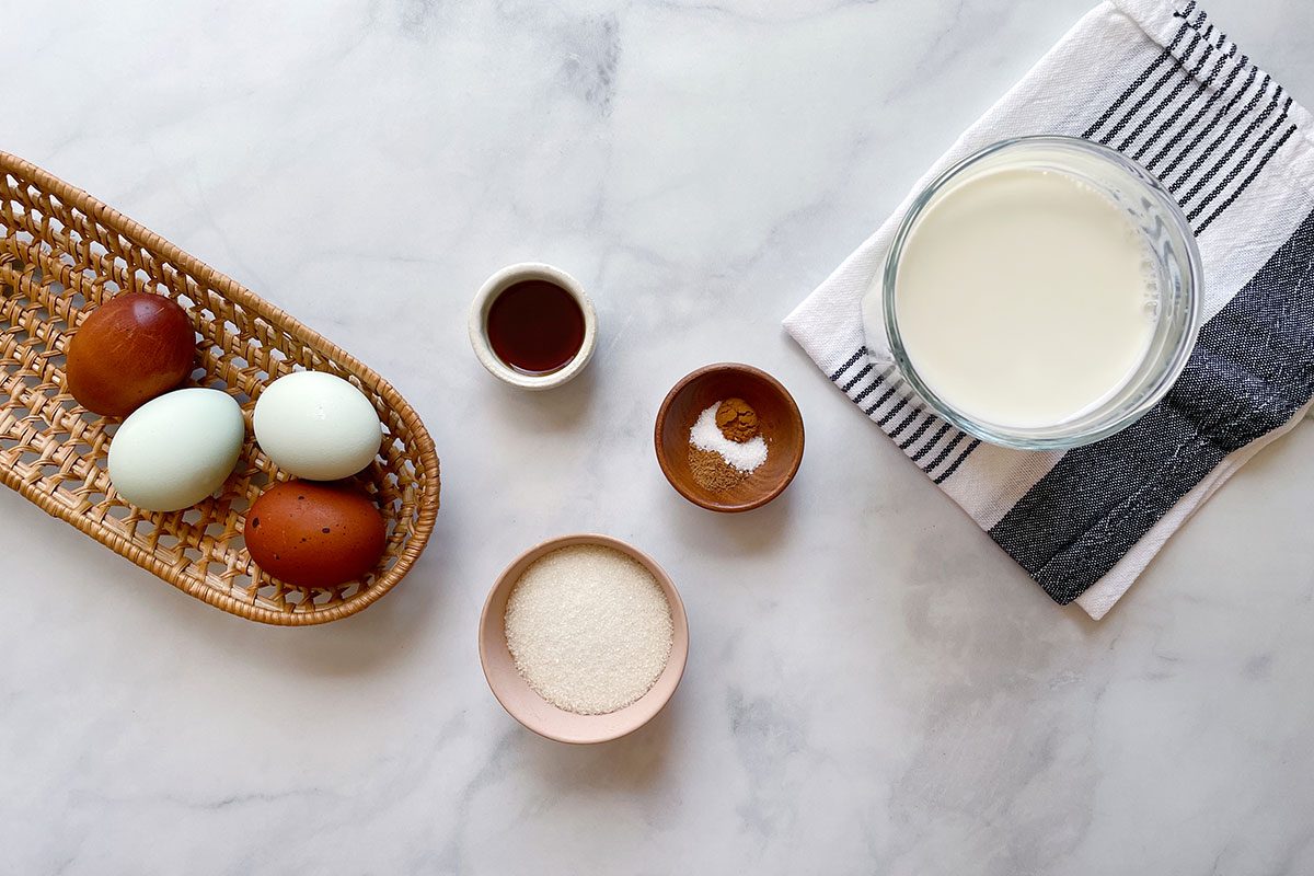 Ingredients to make Taste of Home's Baked Egg Custard laid out on a white marble background
