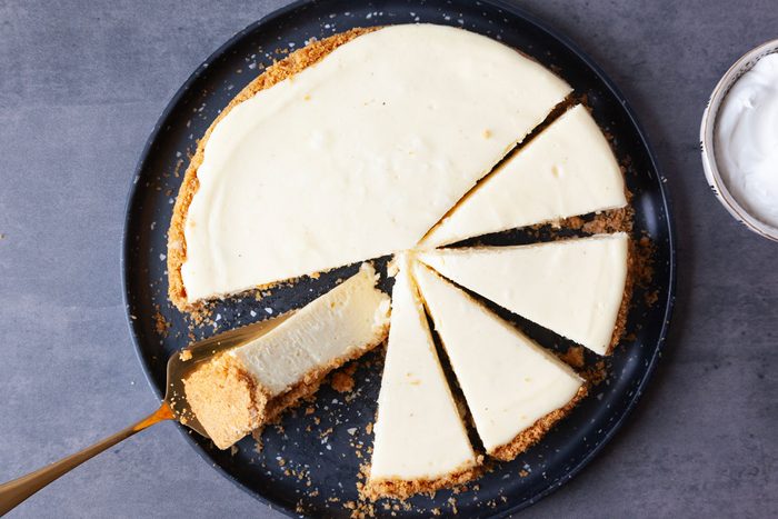 Full yield of Taste of Home Eggnog Cheesecake on a black serving plate with a gold cake server and small bowl of whipped cream
