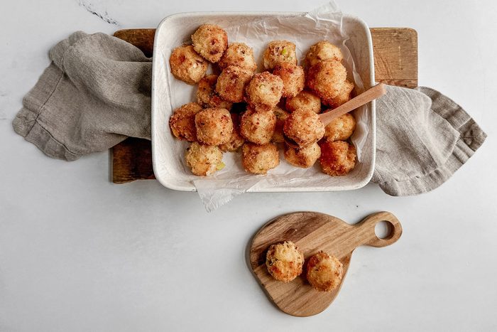Taste of Home fried mashed potato balls in a ceramic tray on a linen napkin on a wooden board on a marble surface.