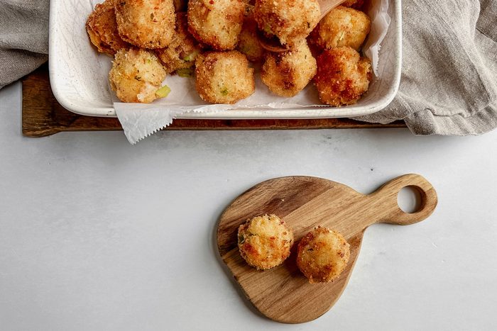 Taste of Home fried mashed potato balls in a ceramic tray on a linen napkin on a wooden board on a marble surface. Taste of Home fried mashed potato balls on a mini wooden board.