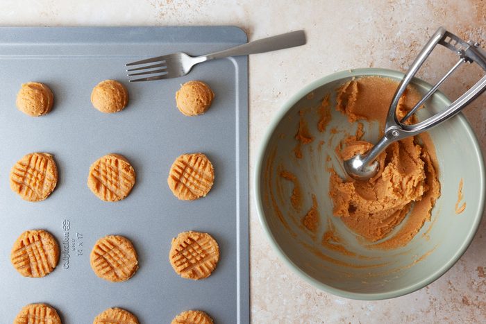 Process shot of Taste of Home Gluten-Free Peanut Butter Cookies, being scooped onto a baking shoot and pressed flat with a fork