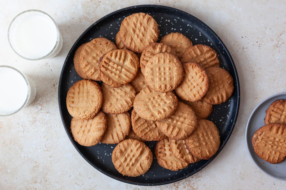 Full yield of Taste of Home Gluten-Free Peanut Butter Cookies on a black serving platter with two glasses of milk and a small plate