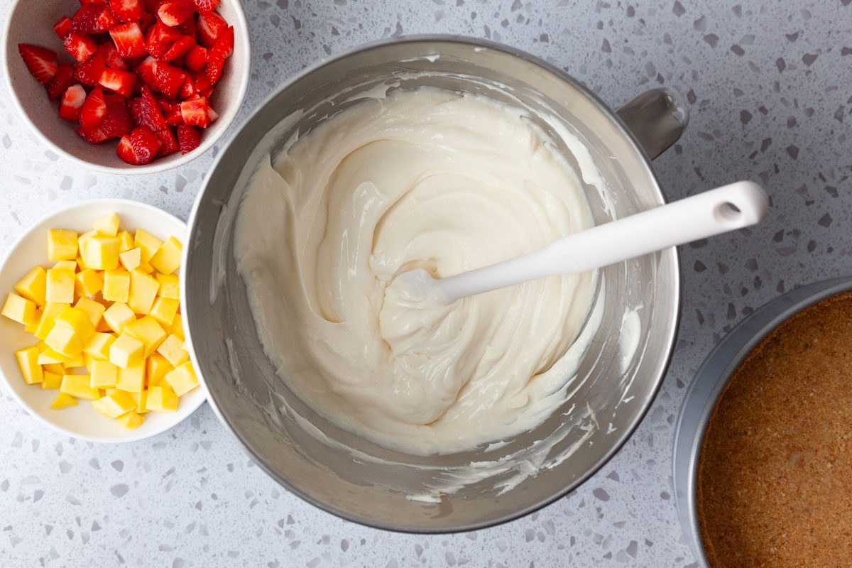 Step 3 of Taste of Home Mango Cheesecake is to make the cream cheese mixture and then stir in the strawberries and mangoes before pouring into the crust