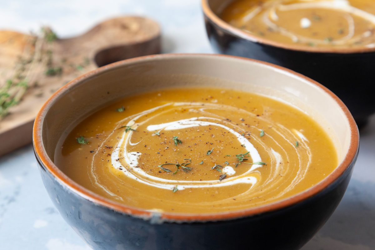 two single servings of butternut squash soup with a sour cream and fresh thyme garnish