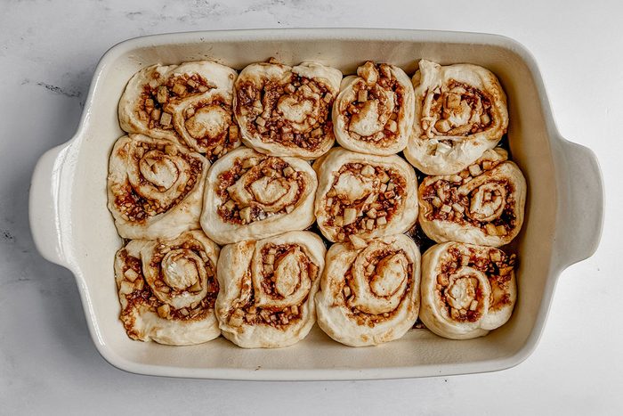 Unbaked Taste of Home apple cinnamon rolls in a white baking dish on a marble surface.