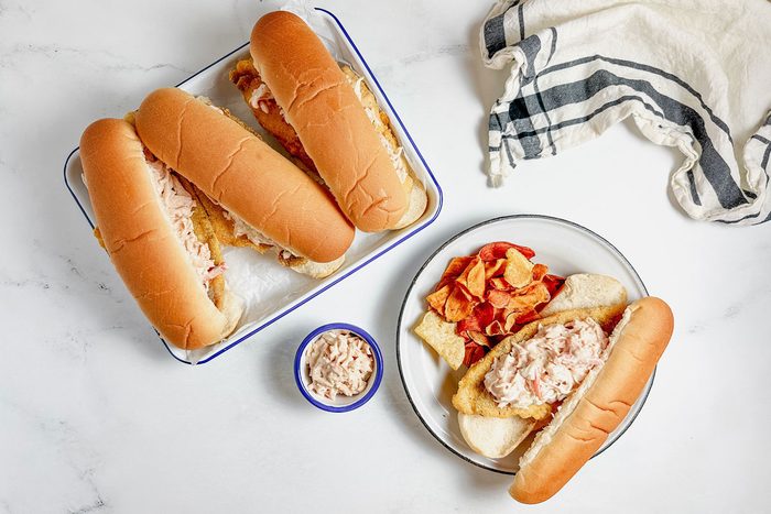 Taste of Home Catfish Po'boy on enamel tray and plate next to a striped napkin on a marble surface.