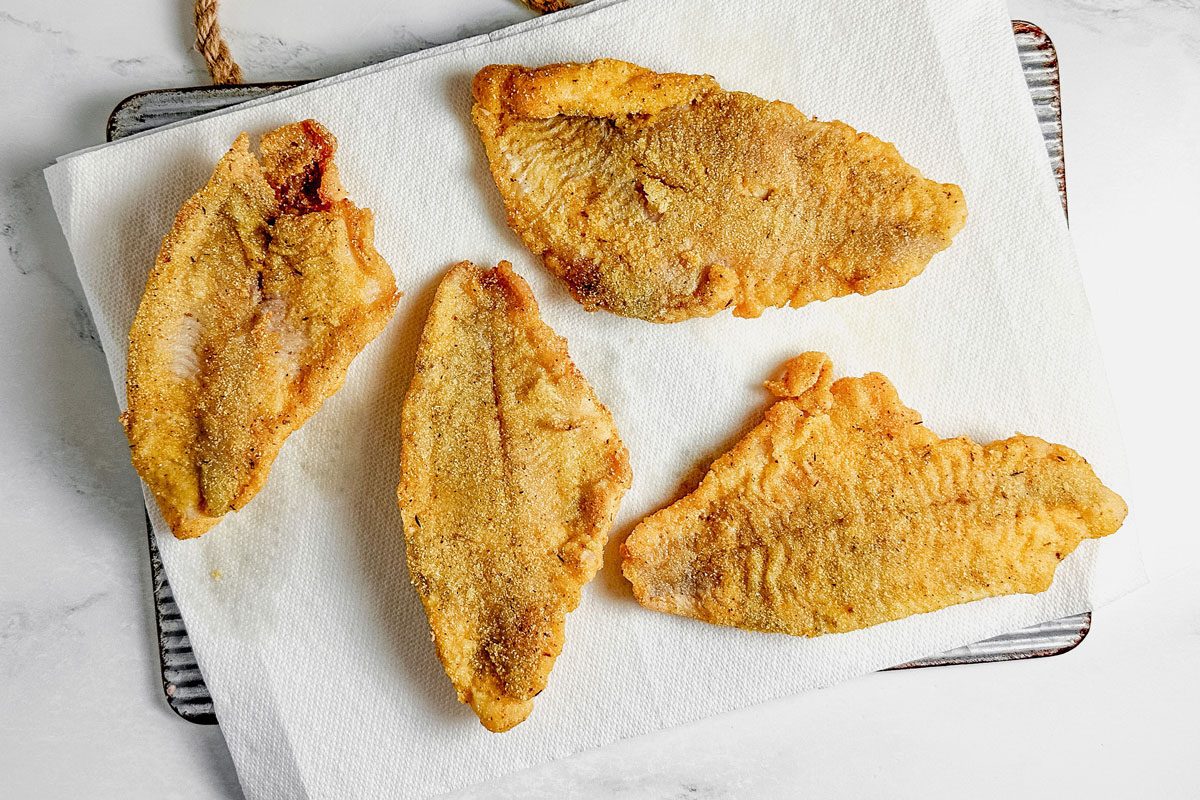 Fried catfish for Taste of Home Catfish Po'boy on a paper towel lined metal board on a marble surface.