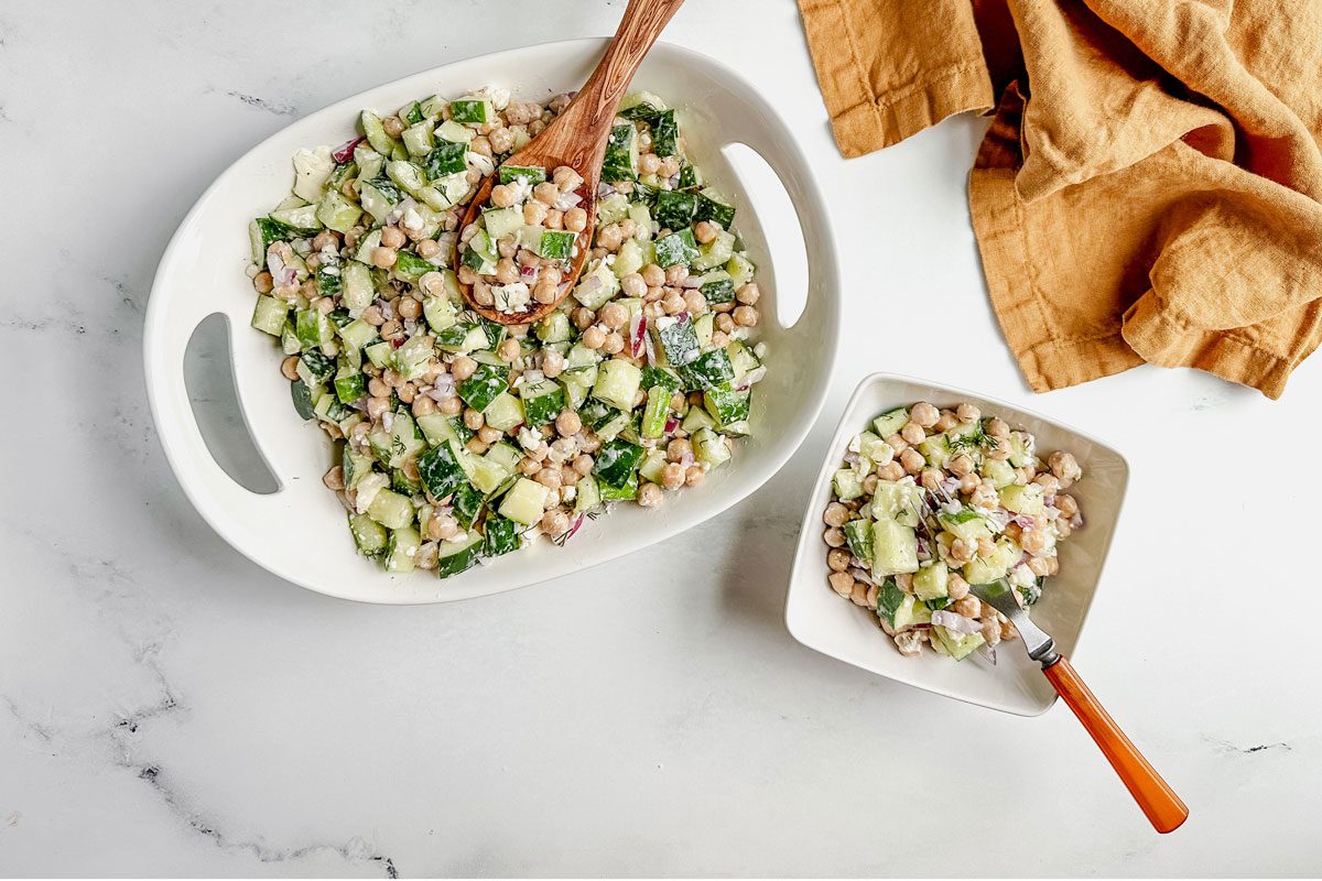 Taste of Home chickpea cucumber salad in white ceramic bowls with linen napkin on a marble surface.