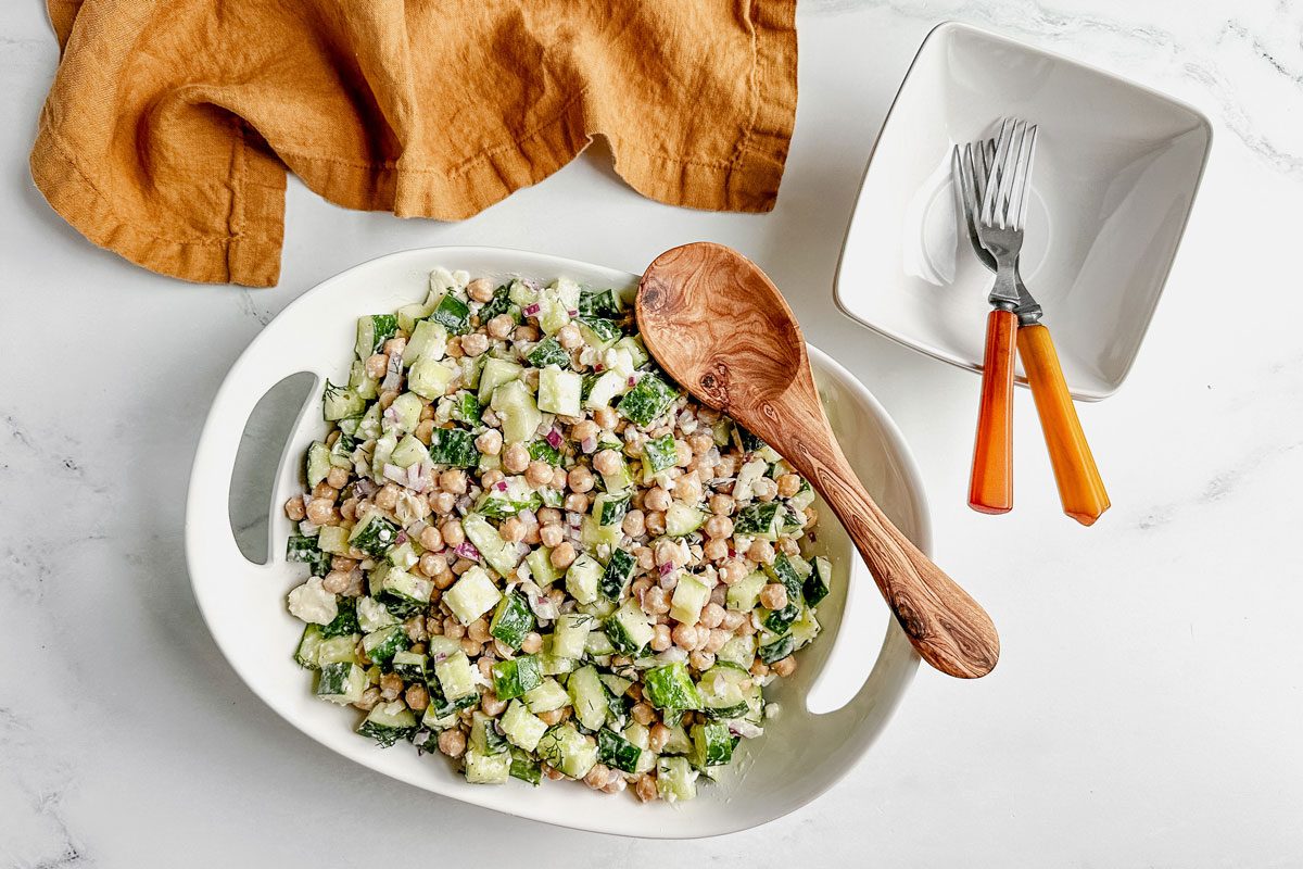 Taste of Home chickpea cucumber salad in a white ceramic bowl with linen napkin on a marble surface.