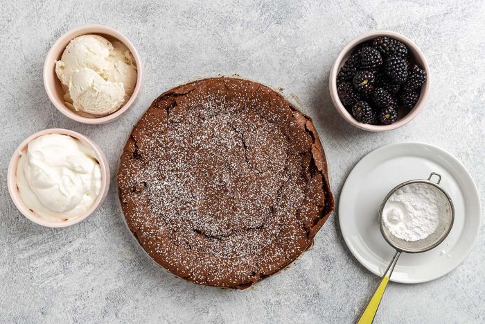 Taste of Home Chocolate Olive Oil Cake recipe photo of the baked cake topped with confectioners' sugar with berries, whipped cream and ice cream on the side.